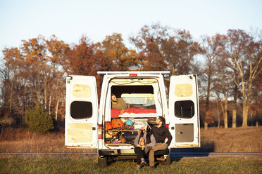 Couple looking at friend relaxing in camper van - CAVF39935