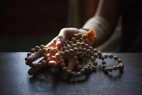 Cropped image of woman holding prayer beads in darkroom at home - CAVF39963