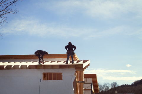 Arbeiter bauen ein Hausdach gegen den Himmel an einem sonnigen Tag, lizenzfreies Stockfoto