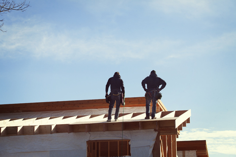Niedriger Blickwinkel von Arbeitern, die auf einem Dachbalken stehen, gegen den Himmel, lizenzfreies Stockfoto
