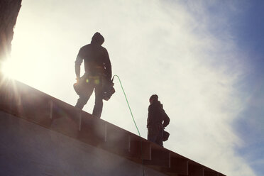 Niedriger Blickwinkel von Bauarbeitern, die auf einem Dachbalken stehen, gegen den Himmel - CAVF39986