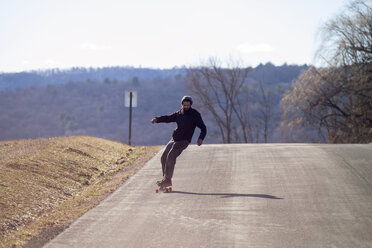 Full length of man skateboarding on country road during vacation - CAVF39989