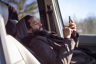Seitenansicht eines Mannes, der ein Smartphone benutzt, während er im Auto sitzt - CAVF39990