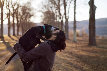 Side view of affectionate man and dog at field during vacation - CAVF39996