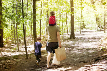 Rückansicht eines Vaters, der mit seinem Sohn und seiner Tochter auf einem unbefestigten Weg inmitten eines Waldes spazieren geht - CAVF40003