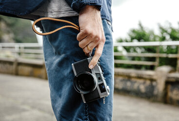 Mittelteil eines jungen Mannes, der eine Kamera hält, während er auf der Straße steht - CAVF40015