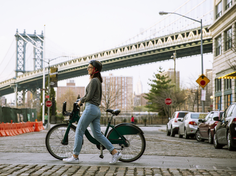 Seitenansicht einer Frau mit einem Lastenfahrrad auf der Straße mit der Manhattan Bridge im Hintergrund, lizenzfreies Stockfoto