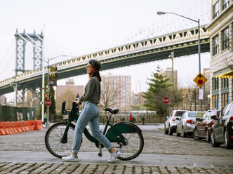 Seitenansicht einer Frau mit einem Lastenfahrrad auf der Straße mit der Manhattan Bridge im Hintergrund - CAVF40026