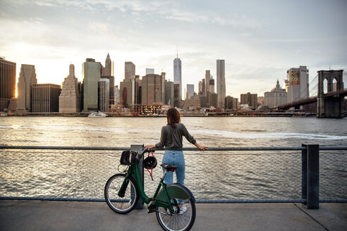 Rückansicht einer Frau mit Fahrrad, die auf einem Aussichtspunkt stehend auf die Stadt blickt - CAVF40027