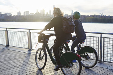 Friends riding bicycle on promenade by river - CAVF40038