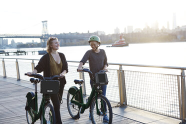 Lächelnde Freunde mit Fahrrädern auf der Promenade am Fluss - CAVF40039