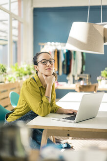 Porträt einer Modedesignerin, die in ihrem Atelier mit einem Laptop am Schreibtisch sitzt - MOEF01018