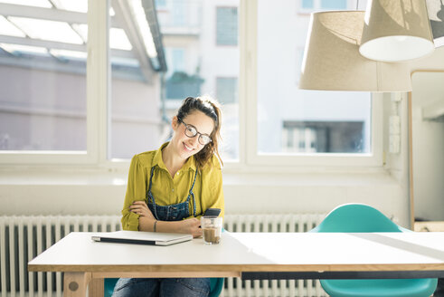Lächelnde Freiberuflerin sitzt am Schreibtisch in ihrem Studio - MOEF01021