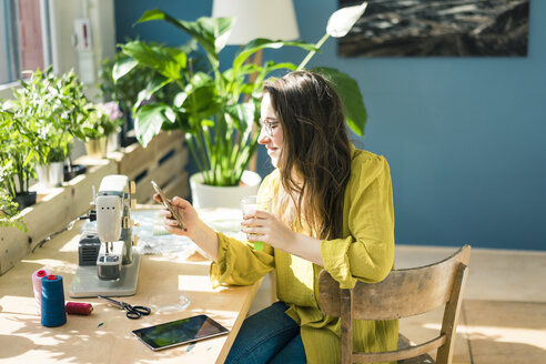 Modedesignerin sitzt am Schreibtisch in ihrem Atelier und benutzt ihr Smartphone - MOEF01028