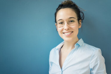 Portrait of smiling young woman wearing glasses in front of blue wall - MOEF01034