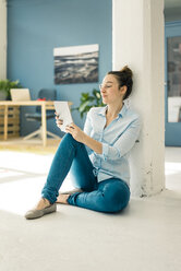 Junge Freiberuflerin sitzt in ihrem Atelier auf dem Boden und benutzt ein Tablet - MOEF01036