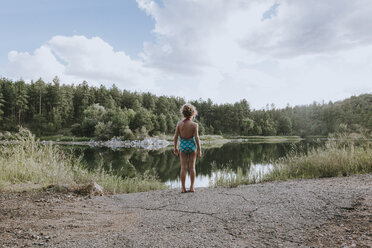 Rückansicht eines Mädchens in Badekleidung, das am Seeufer vor einem bewölkten Himmel steht - CAVF40104