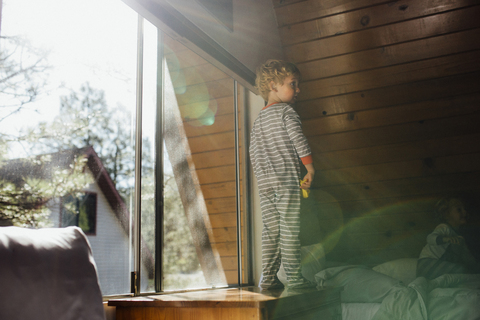 Junge steht auf dem Tisch, während seine Schwester zu Hause auf dem Bett sitzt, lizenzfreies Stockfoto