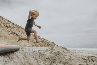 Playful boy jumping on sand at beach - CAVF40121