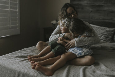 Frau umarmt Kinder auf dem Bett sitzend - CAVF40146
