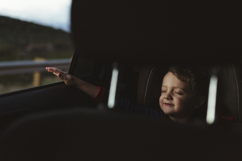 Süßer Junge mit geschlossenen Augen genießt Road Trip durch Fahrzeugsitz gesehen, lizenzfreies Stockfoto