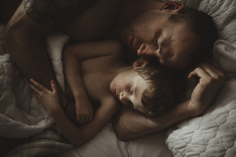 Hohe Winkelansicht von Vater und Sohn schlafend auf dem Bett, lizenzfreies Stockfoto