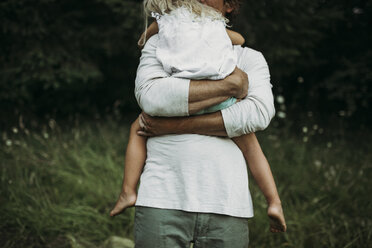Mittelteil eines Vaters, der seine Tochter auf einer Wiese umarmt - CAVF40174