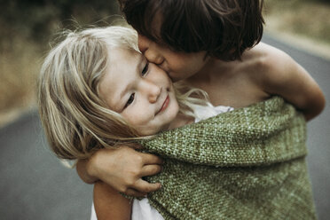 Close-up of brother kissing sister while standing on country road - CAVF40182