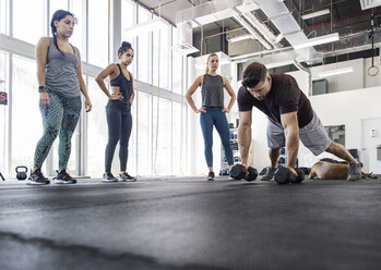 Instructor explaining athletes by doing push-ups using dumbbells in crossfit gym - CAVF40241