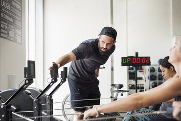 Ausbilderin überprüft Rudergerät, während Frauen im Crossfit-Fitnessstudio trainieren - CAVF40247