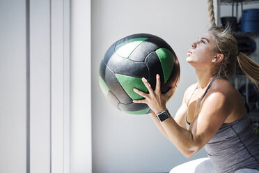 Entschlossener weiblicher Athlet, der mit einem Medizinball im Crossfit-Fitnessstudio trainiert - CAVF40274