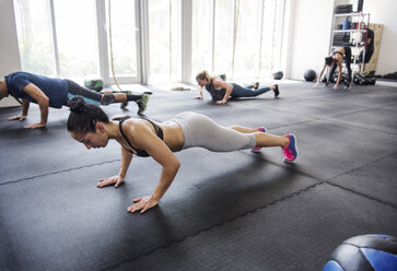 Determined athletes doing push-ups in brightly lit crossfit gym - CAVF40279