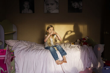 Mädchen macht Herzform mit Händen, während sie auf dem Bett zu Hause sitzt - CAVF40299