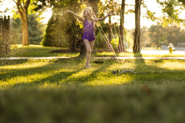 Happy girl playing in sprinkler at backyard - CAVF40310