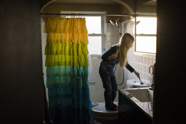 Mädchen reinigt Toilettenspülung mit Toilettenbürste im Badezimmer - CAVF40326