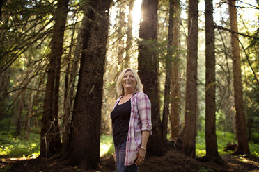 Glückliche reife Frau steht gegen Bäume im Wald - CAVF40342