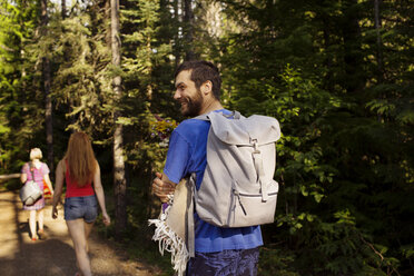 Lächelnder Mann mit Rucksack, der mit seiner Mutter und seiner Schwester durch einen Wald spaziert - CAVF40346