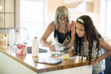 Enkelin und Großmutter bereiten Essen zu, während sie in der Küche auf einen Tablet-Computer schauen - CAVF40349