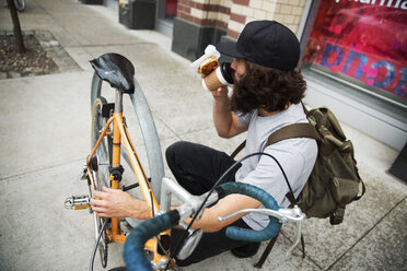 Blick von oben auf einen Mann, der Kaffee trinkt, während er auf dem Gehweg neben einem Fahrrad hockt - CAVF40378