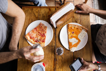 Mittelteil von Freunden beim Pizzaessen am Holztisch im Restaurant - CAVF40380