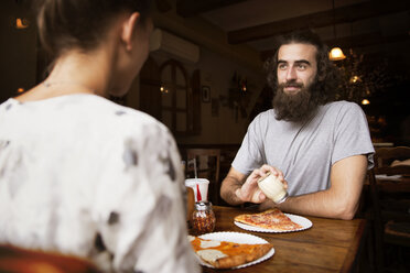 Mittelteil von Freunden beim Pizzaessen am Holztisch im Restaurant - CAVF40382