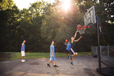 Spieler spielen Basketball auf dem Platz gegen Bäume an einem sonnigen Tag - CAVF40388
