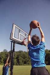 Boys playing basketball by trees against clear sky - CAVF40389