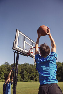 Jungen spielen Basketball zwischen Bäumen gegen den klaren Himmel - CAVF40389