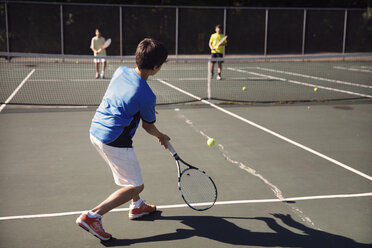Jungen spielen Tennis auf dem Platz gegen den Zaun an einem sonnigen Tag - CAVF40396