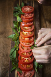 Ausgeschnittenes Bild einer Frau, die Minzblätter in einem Tomatensalat am Tisch arrangiert - CAVF40416
