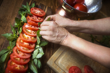 Beschnittenes Bild einer Frau, die Tomatensalat mit Minzblättern am Tisch garniert - CAVF40417