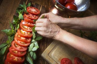 Cropped image of woman garnishing tomato salad with mint leaves at table - CAVF40417