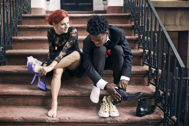 Paar zieht Schuhe aus, während es auf einer Treppe sitzt - CAVF40439