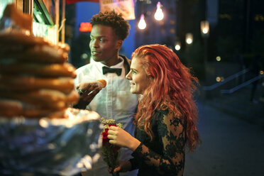 Couple eating hot dog while standing on city street at night - CAVF40448